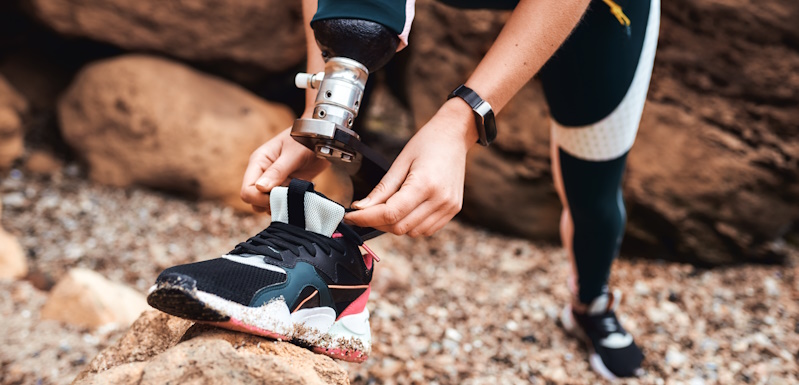 person with a prosthetic leg tying their shoe on a trail
